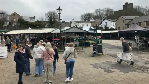 People wearing coats standing by market stalls at Clitheroe Market.