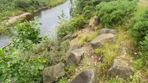Tweed Forum A pile of large stones have been placed at the bend of a river to prevent erosion and flooding. The shallow river arches away from the stones 