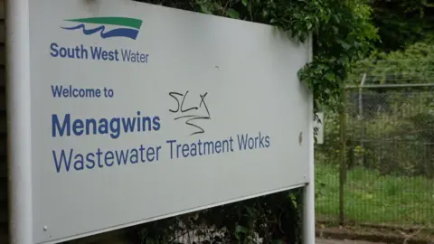 A sign at the waterworks' entrance which has the South West Water logo and the words: Menagwins Wastewater Treatment Works