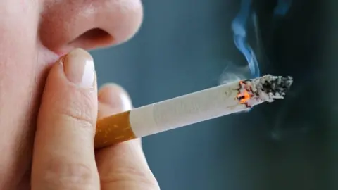 Getty Images A close-up of a cigarette, held between two fingers and being inhaled.
