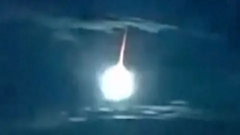 A white fireball with an orange tail illuminates an otherwise dark blue sky above Japan.