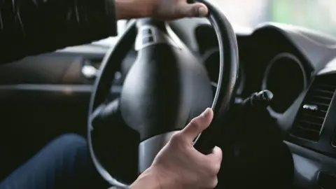 Generic photo of a man's hands on a driving wheel, steering the car.