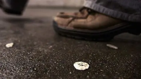 Chewing gum on street with man's shoes in background.