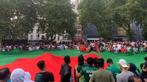 Giant flag of Bangladesh in Altab Ali park being held, with large crowds in the background