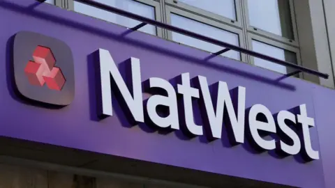 Getty Images Close up of a NatWest sign. The background is purple and the text is white. It also features a small navy and red logo on the left.