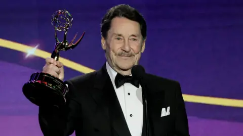 Getty Images Peter Cullen in a dinner jacket holding up his Emmy Award on stage