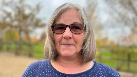 Alison Thompson, looking at the camera, standing within the burial ground