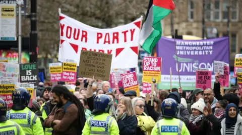 EPA Counter-protestors hold aloft various placards and banners in a demonstration against Britain First. Police officers with helmets stand in front of them.