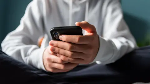 Close up of hands of teen boy in a white hoodie texting on phone.