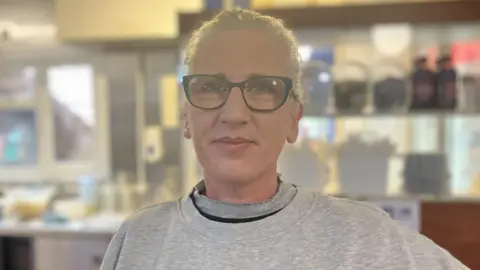 Sam Dixon-French/BBC A headshot of a woman with long, white hair. She is wearing black frame glasses and a grey jumper.