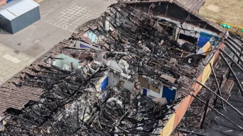 An aerial shot shows a fire-damaged school roof.