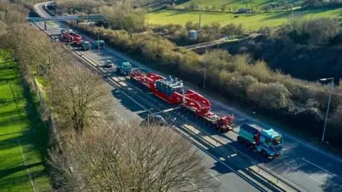 A shot of a two large transport vehicles travelling up a two-lane motorway.