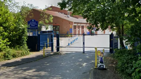 A street view of St. Monica's Catholic Elementary School taken from outside its blue doors. The school building is visible on the other side of the doors.