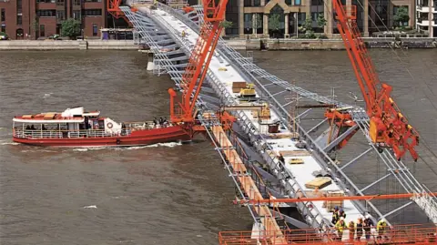 Nigel Young, Foster + Partners The bridge in construction, with orange machinery seen working on the structure.