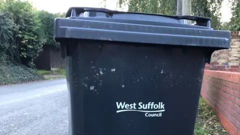 Vikki Irwin/BBC A general view of a West Suffolk black waste bin on a pavement. A road passes next to it.