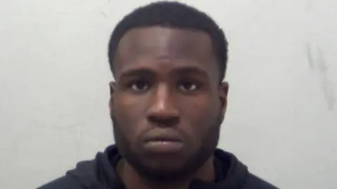Noble Nwokocha in police custody. He has short black hair and is wearing a black hoody.
