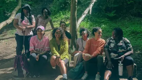 Leanne Wharton A group of eight women sat down after a walk. They are wearing hiking gear.