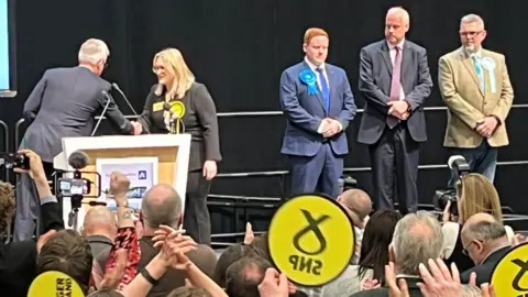 The SNP's Karen Adam winning her election seat, with other candidates looking on.