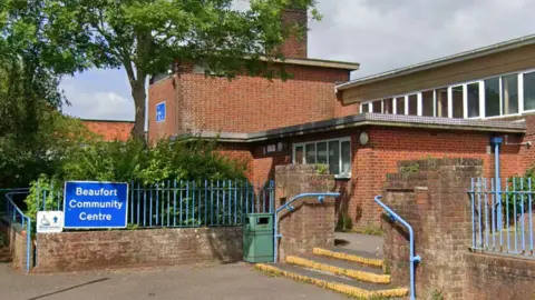 Beaufort Community Centre is a large red brick building with multiple floors extended over three main structures. Outside is a large blue sign saying Beaufort Community Centre.