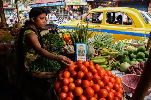 NurPhoto via Getty Images A vegetable vendor waits for customers, displaying a barcode for Paytm, an Indian cellphone-based digital payment platform, at a market in Kolkata.