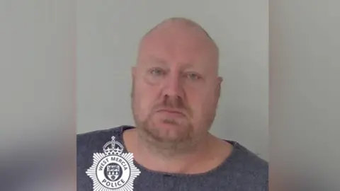 West Mercia Police Police mugshot showing a bald man with short facial stubble  wearing a blue T-shirt and looking at the camera