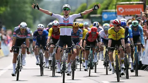 Tadej Pogacar celebrates with his arms outstretched as he crosses the line