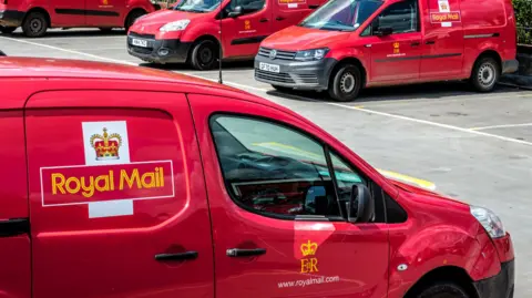 Getty Images A close-up picture of a red van with the Royal Mail logo and title on the side. It is in a car park with three similar vans beyond.