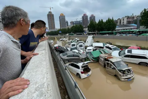 AFP People look out at cars sitting in floodwater after heavy rain hit the city of Zhengzhou in China's central Henan province, on 21 July 2021