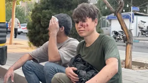 Two young men nurse injuries on a roadside in Iran.