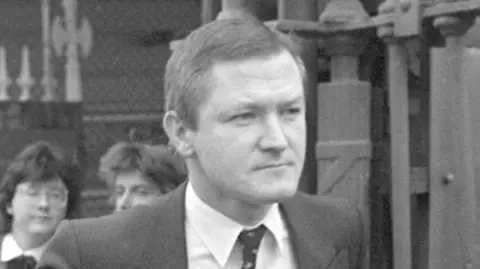 A black and white image of Pat Finucane. He is wearing a suit and tie.