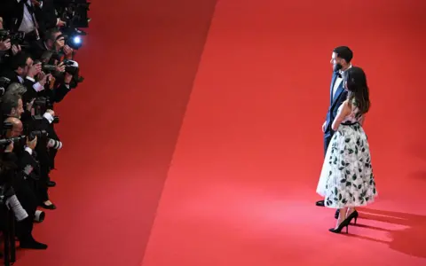 SAMEER AL-DOUMY / AFP / GETTY IMAGES A man and a woman pose for photographers as they walk down a red carpet.