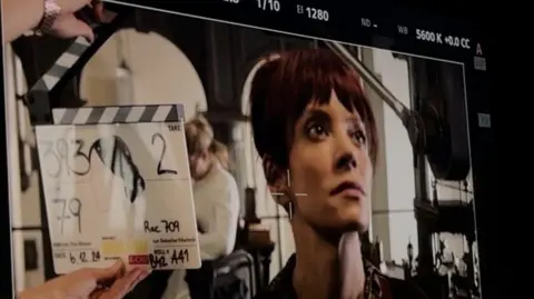 A behind-the-scenes shot from Night and Day with the view from a monitor showing the actress Lily Allen in character and looking to the right of the screen and with a clapperboard beside her head.