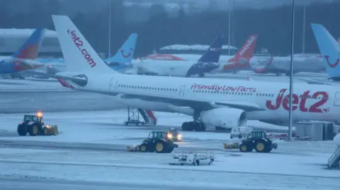 Staff use tractors to help clear snow from around aircraft at Manchester Airport