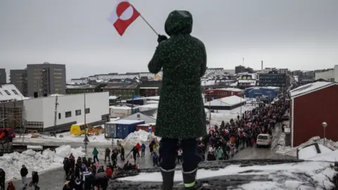 A woman waves a Greenlandic flag as people attend a protest against President Donald Trump's demand that the Arctic island be ceded to the US, in Nuuk, the capital of Greenland