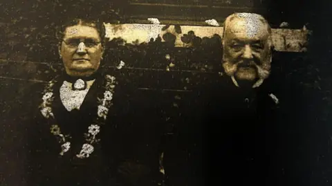 A faded black and white photograph shows a Victorian-era couple.