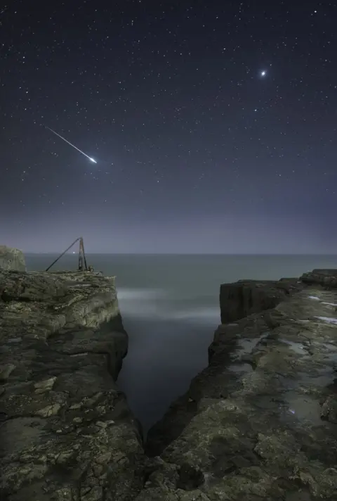 Rob Bowes A shooting star flashes across the sky over the craggy landscape