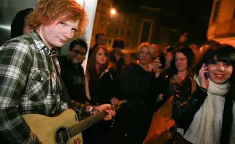 Jen O'Neill Ed Sheeran with an acoustic guitar standing in the street outside a pub with an audience of mostly female fans