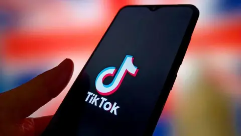 A hand holds a phone displaying the TikTok app