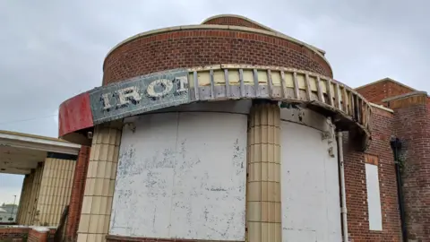 Great Yarmouth Preservation Trust Outside the Iron Duke which appears run down. The sign above it is worn and faded to only read 'IRO'. It is also falling down. The building is brick and the windows have all been boarded up. 