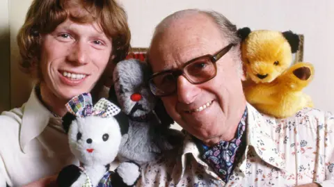 Sooty with Matthew Corbett and Harry Corbett : 1977 : Picture shows - Matthew Corbett and his father Harry Corbett with the glove puppets, 'Soo' (a panda), 'Sweep' (a dog) and 'Sooty' (a bear), 1977. (L-R) Corbett, Matthew ; Soo : Sweep ; Corbett, Harry ; Sooty