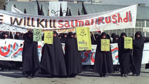 Getty Images Fotografía del 17 de febrero de 1989 de mujeres iraníes sosteniendo pancartas que decían "Acebo Corán" y "Mataremos a Salman Rushdie" durante una manifestación en Teherán contra el autor de "Los versos satánicos". (Foto de NORBERT SCHILLER/AFP) (Foto de NORBERT SCHILLER/AFP vía Getty Images)