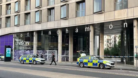 Three police cars in front of a police cordon.