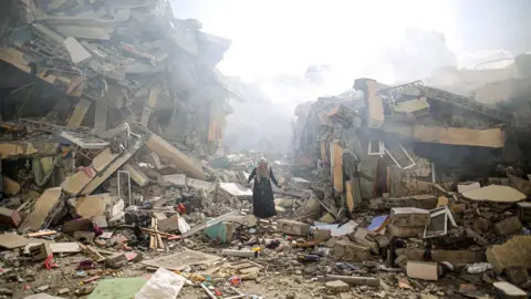 Mustafa Hassouna Woman standing in the rubble of fallen buildings in Gaza