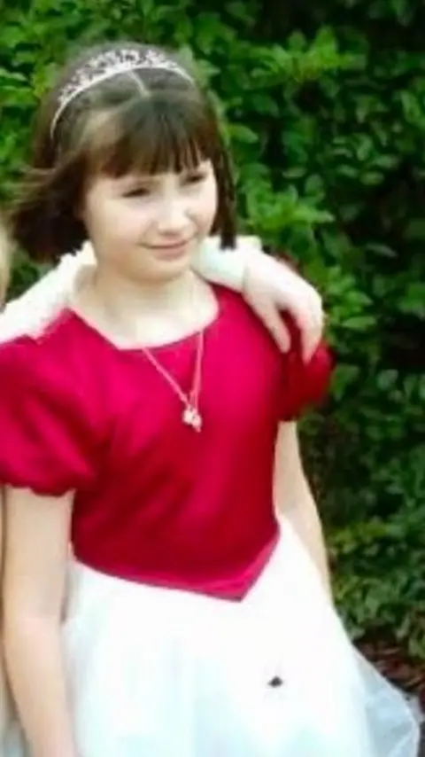 Sarah Cooper-Lesadd A girl with short dark hair wears a prom-style dress with a satin pink top half and a white tulle skirt.