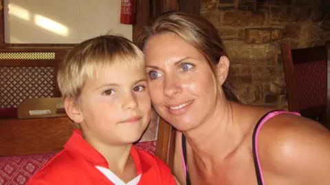 James Hirst A young boy in a red top with a woman leaning against him and smiling