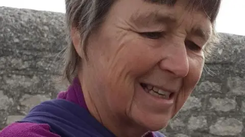 Close up of a woman with short hair, smiling, wearing a purple fleece sweatshirt