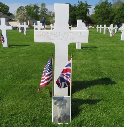 ABMC The grave of Donald Morgart, from Iowa, who died on 23 April 1944, with a British and American flag and his photo