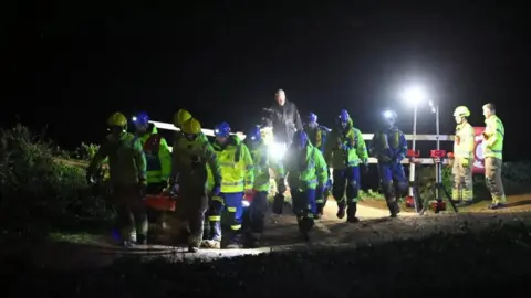 Ground of coastguard and firefighters wearing head torches  carrying a stretcher in the dark on a cliff top 