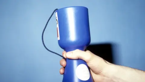 A picture of a hand holding out a blue charity pot. It has two white stickers on it.