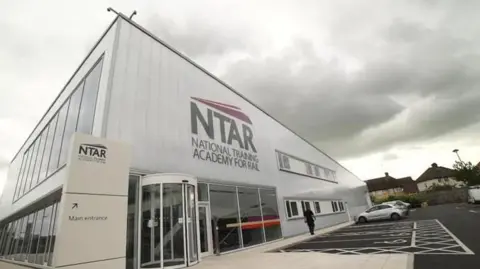 A silver coloured building with glass frontage with "NTAR, National Training Academy for Rail"